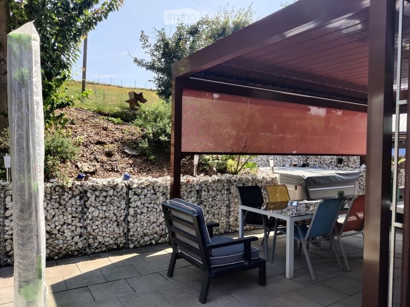 Outdoor patio with a stone wall, a covered seating area, a hot tub, and a dining table with chairs.