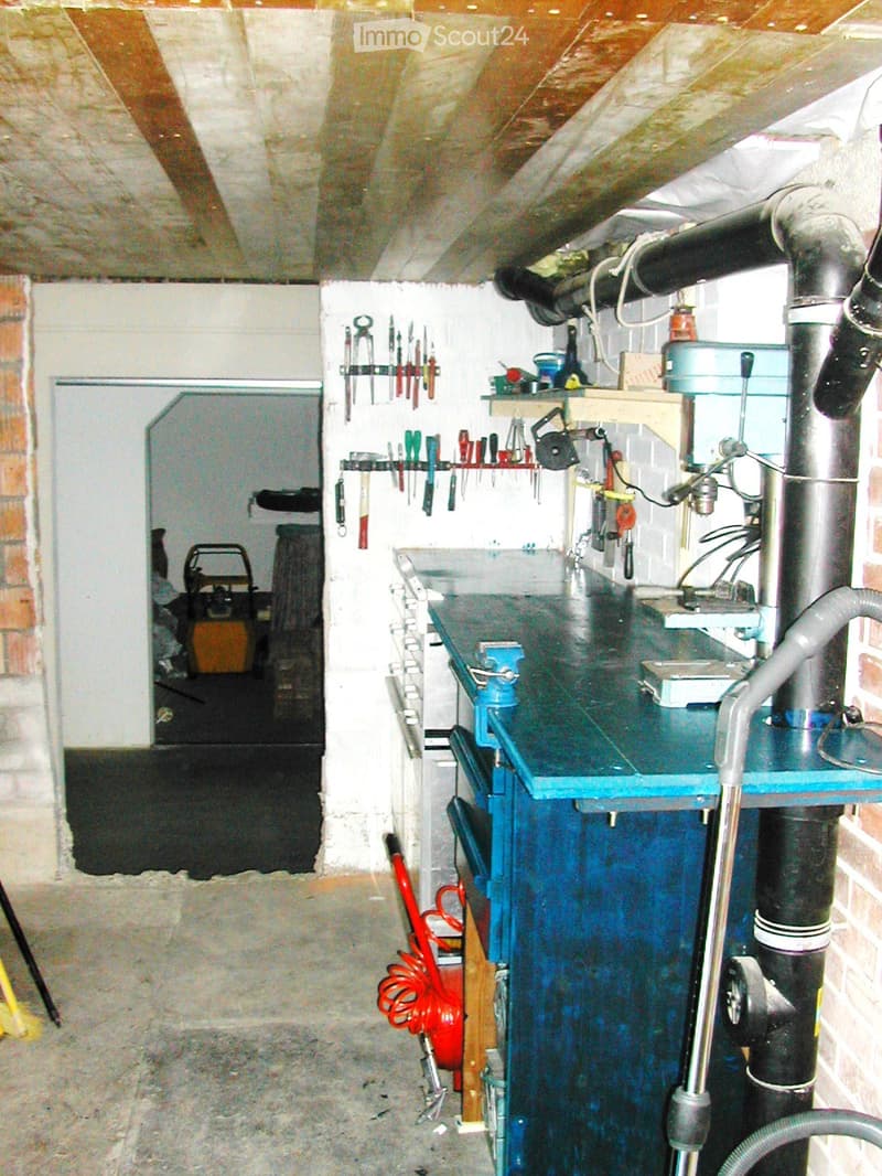 Workshop with a blue worktop, various tools on shelves, a drill, saw, and vacuum cleaner.