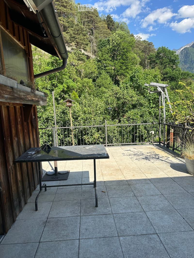 Balcony with tiled floor, metal table, railing, and scenic mountain view.