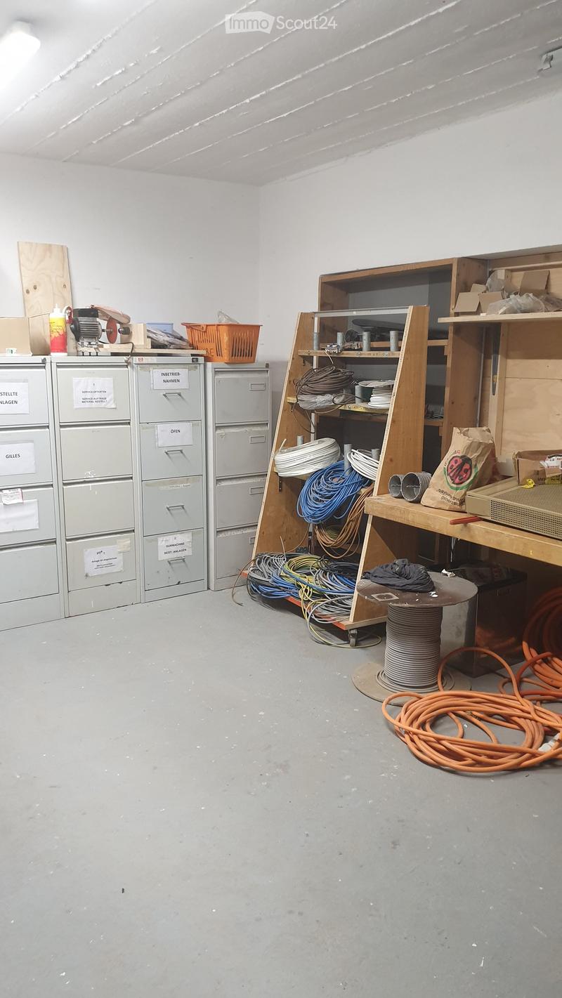 A storage or utility room with file cabinets, wooden shelves, a workbench, and various tools and materials including cables and wooden planks.
