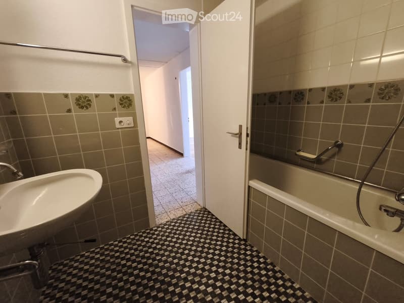 Bathroom with a sink, bathtub, and floral-patterned tiles. The floor has a black and white checkered pattern, and there is a hallway visible in the background.