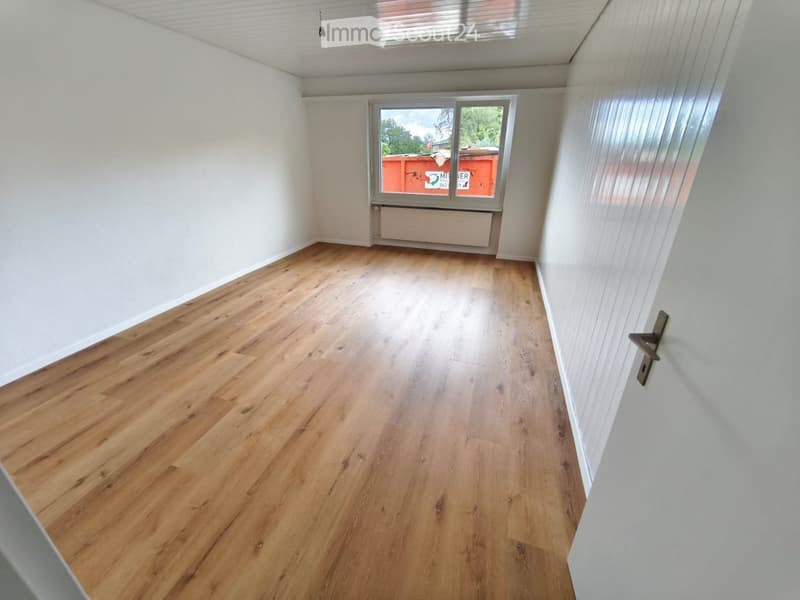 Empty room with wooden flooring, white walls, and a large window showing an outdoor view.