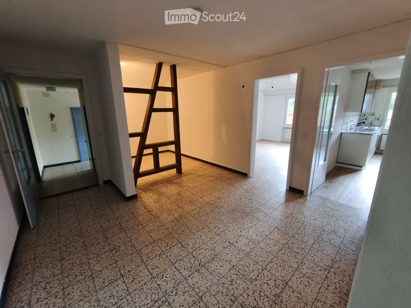 Empty hallway with tiled floor, leading to a kitchen area with white cabinets and a sink.