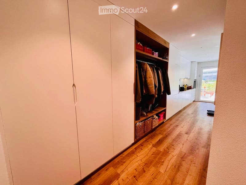 A room with a wooden wardrobe, baskets, shoes, and coats. The floor is wooden, and there is a door leading to another room.