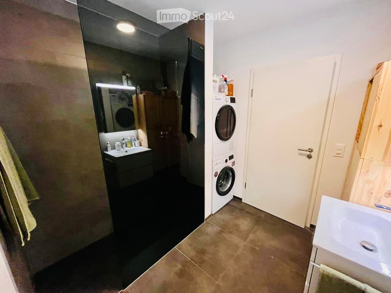Bathroom with a mirror, sink, washing machine, dryer, cabinet, towel, bottle, soap, soap dispenser, power outlet, and door.