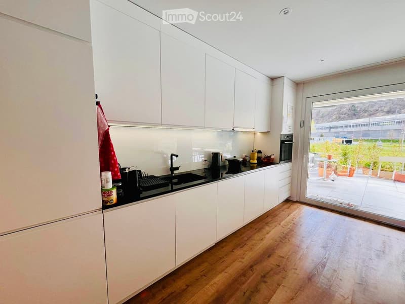 Modern kitchen with white cabinets, black countertops, and wooden floors. Equipped with a sink, faucet, and various kitchen appliances.
