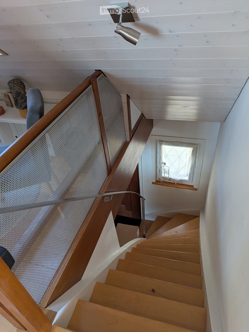 Spiral staircase with wooden steps and a metal railing, leading to a small windowed area with a candle on a shelf.