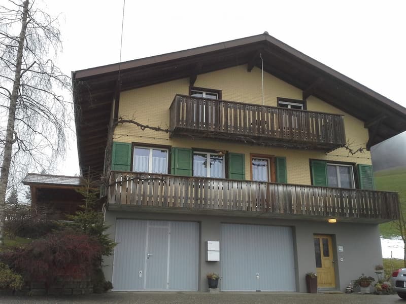 Two-story house with yellow brick facade, green shutters, two balconies, and a garage.