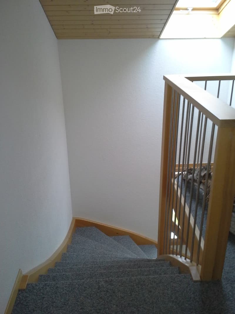 Spiral staircase with wooden handrail and gray carpeted steps, leading to an upper level with a skylight above.