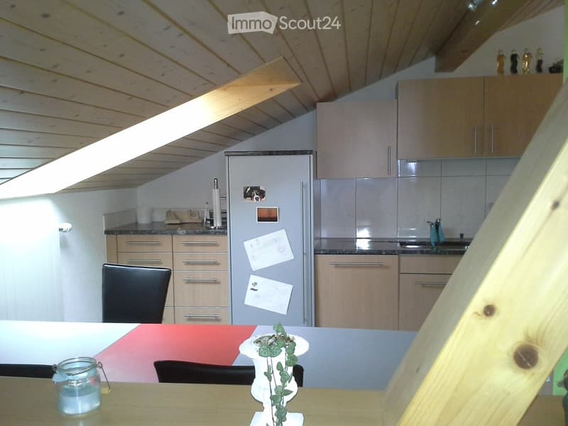 Modern kitchen with light wooden cabinets, stainless steel appliances, and a sleek design. Features a dining area with a table and chairs, a candle, and a vase with greenery.