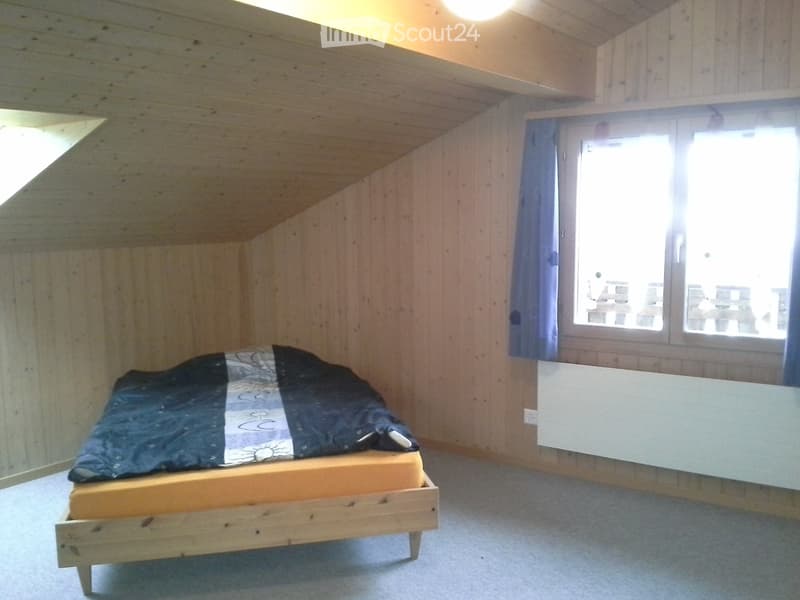Bedroom with wooden walls and ceiling, a single bed with a mattress and duvet, a window with blue curtains, and a radiator below the window.