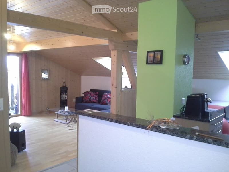 Open-plan living and kitchen area with wooden beams, exposed wooden ceiling, and a mix of modern and rustic furniture.