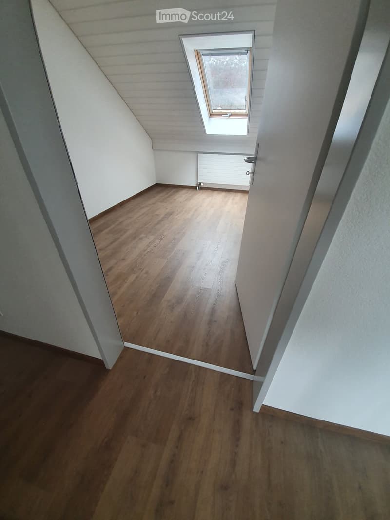 An empty room with wooden flooring and white walls. There is a window and a door.