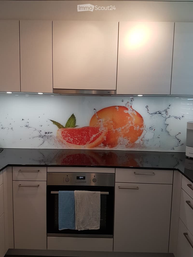 Modern kitchen with white cabinets, black countertops, and a glass splashback with fruit design.