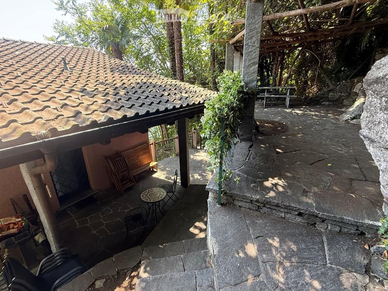 Outdoor patio area with stone flooring, wooden furniture, and a covered section with a tiled roof.