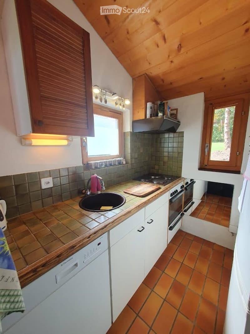 Cozy kitchen with wooden beams, white cabinets, tiled countertops, and a sink. Features include an oven, dishwasher, and wooden cutting board on the counter.