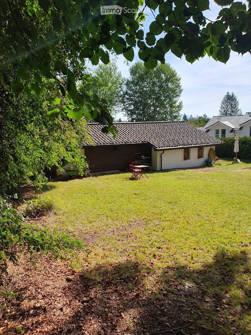 A well-maintained garden with a small wooden house, a table and chairs, surrounded by trees and greenery.