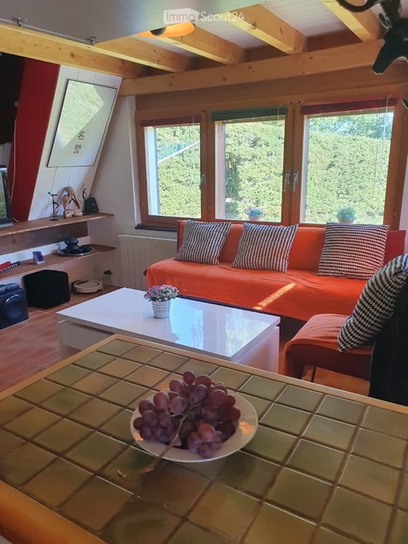 Bright living room with large windows offering a view, orange sofa with black and white striped cushions, white coffee table with a small flower vase, and a bowl of grapes on a glass table.