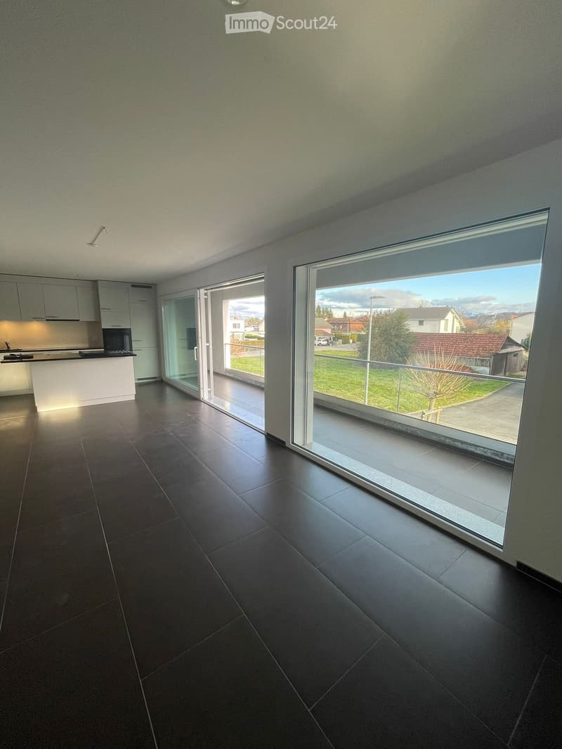 {"visible_features": ["View"],"type": "Living room","description": "Spacious open-plan living area with large windows providing a scenic view of the outdoor landscape. The room features a modern kitchen with white cabinets and a sleek tile floor through