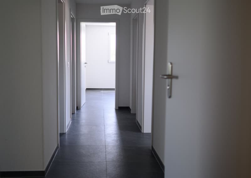 {"visible_features":[],"type":"Hallway","description":"The image shows a long, narrow hallway with white walls and a dark tile floor. The hallway leads to a doorway at the end, which appears to be a room or another area of the property. The hallway has a