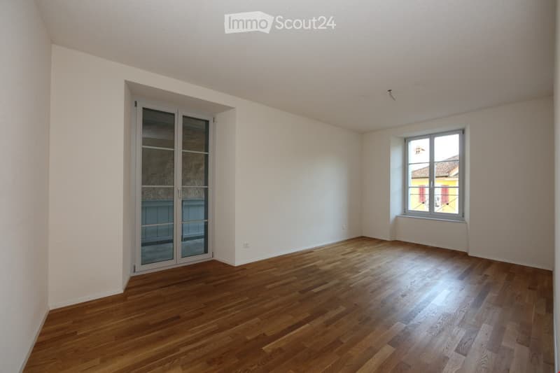 Empty room with wooden flooring, white walls, a large window, and a glass cabinet door.