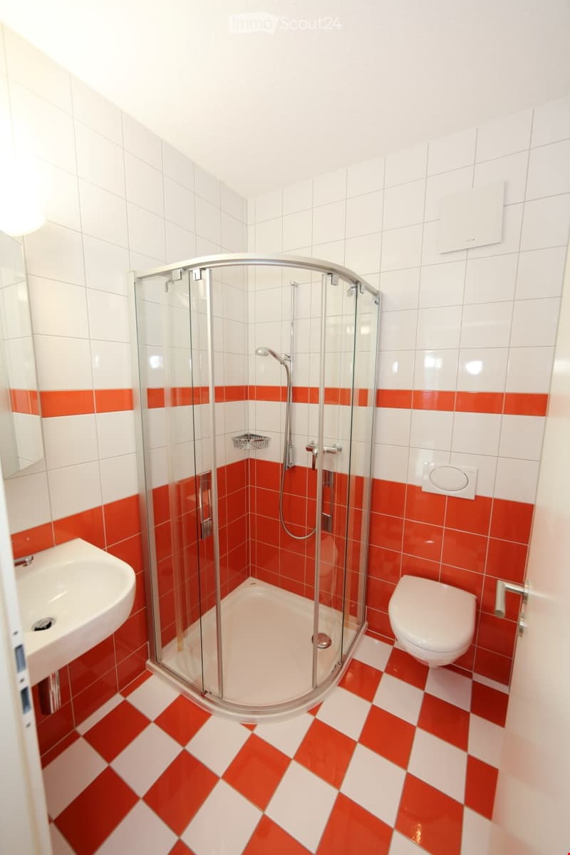 Modern bathroom with white and red tiles, a glass-enclosed shower stall, a sink, and a toilet.