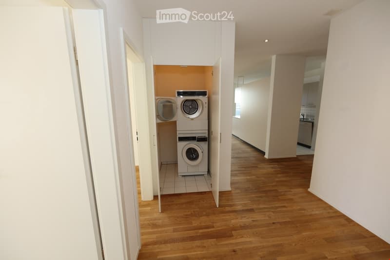Hallway with wooden flooring leading to a room containing a private washing machine and dryer.