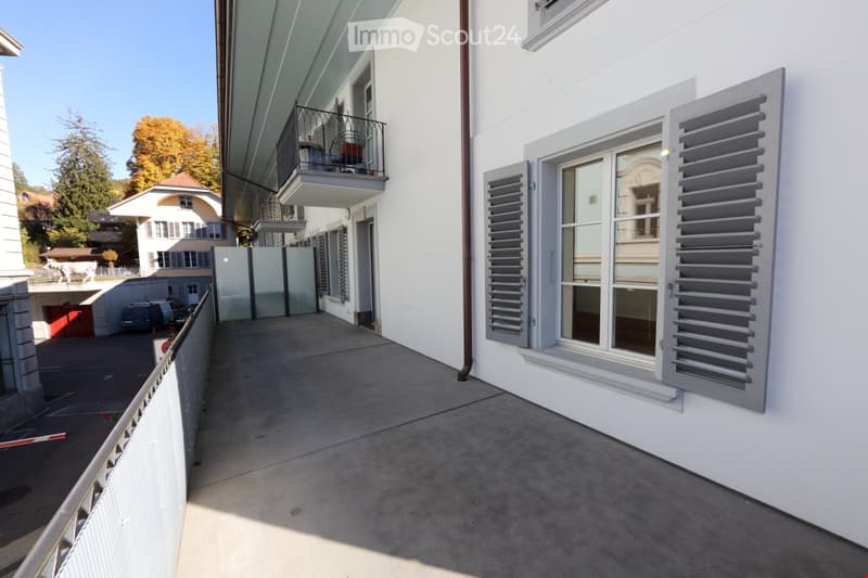 Balcony with metal railing, overlooking a street with parked cars and neighboring buildings.