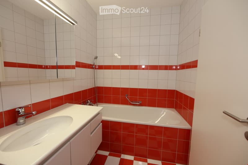 Modern bathroom with white and red tiled walls, a white sink with a chrome faucet, a bathtub, a mirror, and a showerhead.