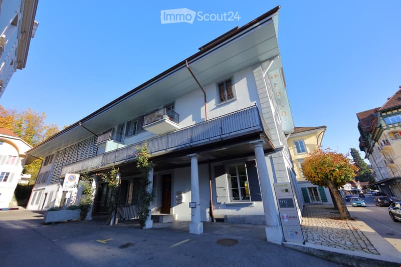 Two-story building with a balcony, white facade, and classic architectural details.