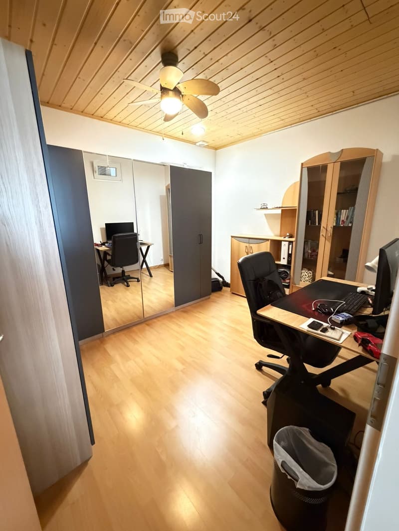 Spacious attic room with wooden floors, two desks, chairs, computers, a large mirror, and a wardrobe.