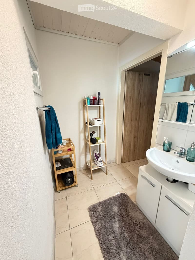 Modern bathroom with a white sink, mirror, towel rack, shelves, and a fluffy rug on the floor.