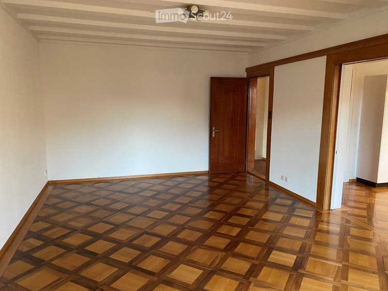 Empty hallway with wooden checkered flooring, white walls, and a ceiling light fixture. Two doors are visible, one leading to another room.