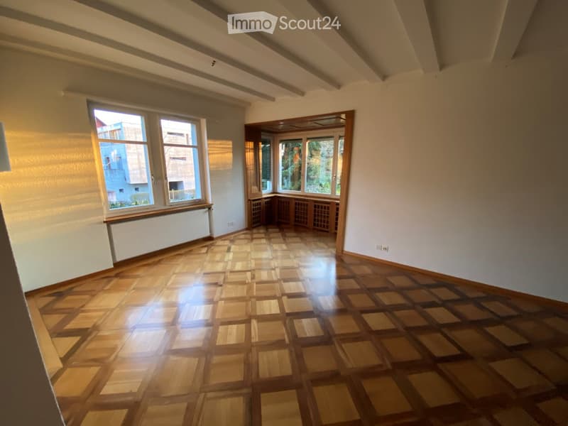 Empty room with wooden parquet flooring, large windows, and exposed wooden beams on the ceiling.