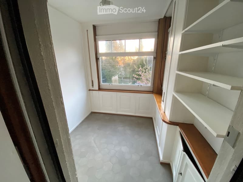 Empty room with white walls, hexagonal tile floor, built-in window seat with wooden trim, and white built-in shelving unit.
