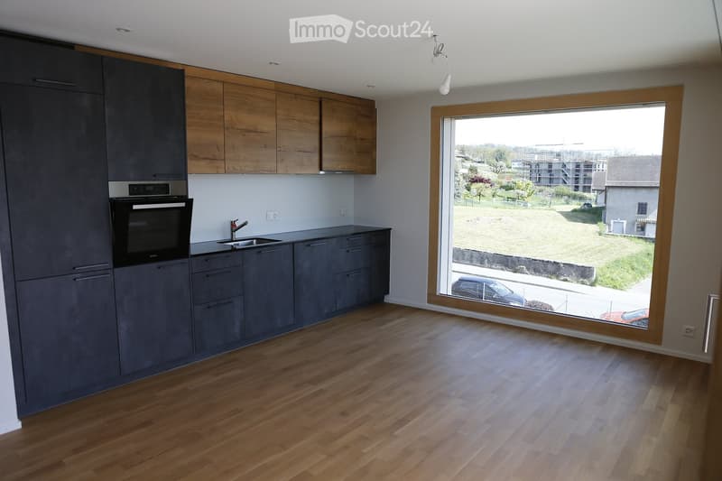 Modern kitchen with grey and wooden cabinets, a large window overlooking a green area, and a wooden floor.