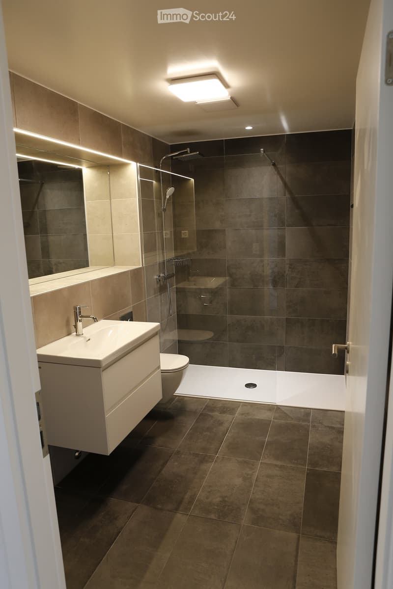 Modern bathroom with a white sink, toilet, glass-enclosed shower, and large mirror illuminated by LED lighting.
