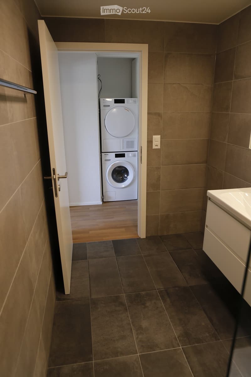 Hallway with tiled floor, open door leading to a room with a stacked washer and dryer unit.