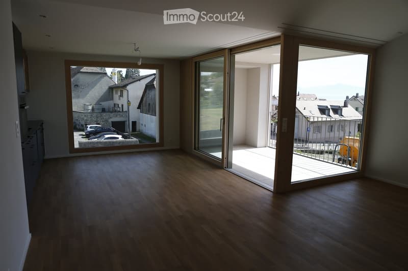 Empty room with wooden flooring, large sliding glass doors leading to a balcony, and a view of the surrounding area.
