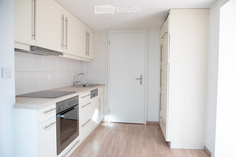 Modern kitchen with white cabinets, stainless steel appliances, and a wooden floor.