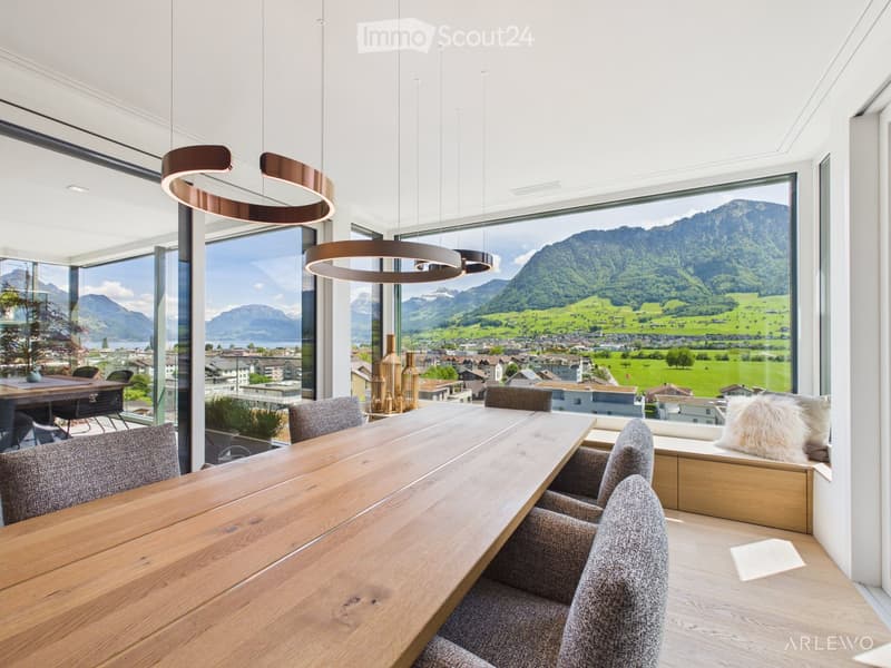 Modern dining room with large windows offering a scenic mountain view, featuring a wooden dining table, chairs, a cushion, and decorative vases.