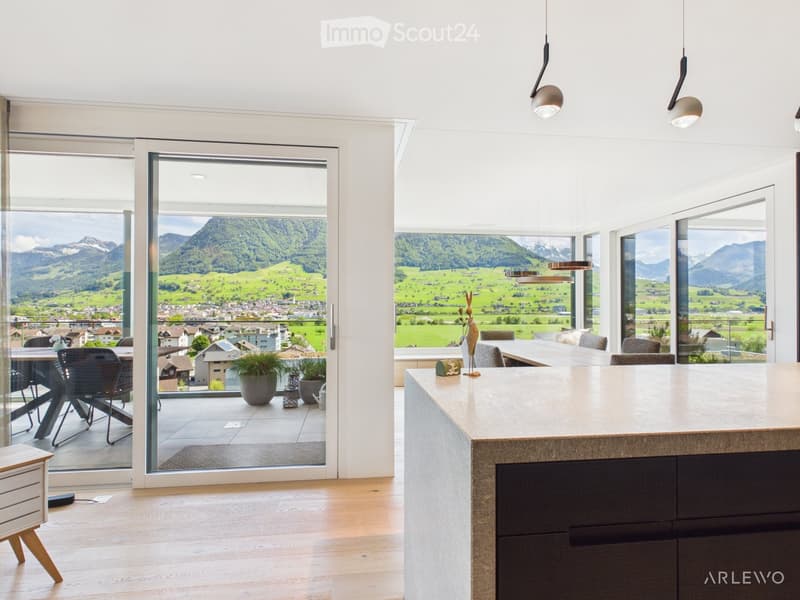 Modern kitchen and dining area with large windows offering a scenic mountain view, featuring a central island, pendant lights, and a dining table with chairs.