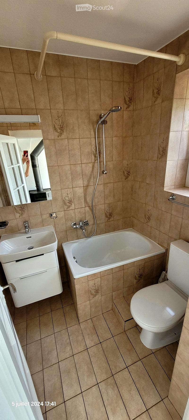 Bathroom with beige tiled walls and floor, featuring a sink, bathtub, toilet, mirror, and showerhead.
