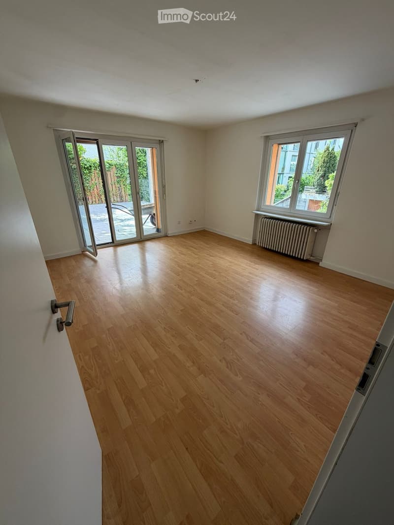 Empty room with wooden flooring, large windows, and sliding glass doors leading to an outdoor area.