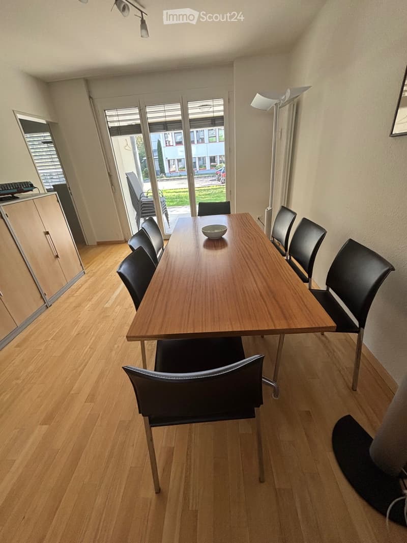 Dining room with wooden floor, large wooden table, black chairs, and a small cabinet.
