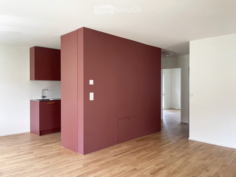 Empty room with wooden flooring, white walls, and a small kitchen area with a sink and cabinets.