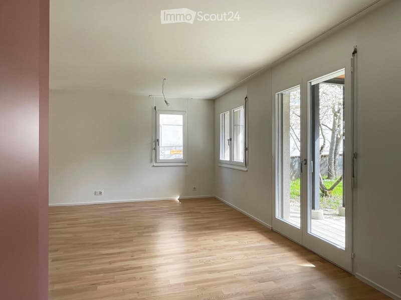 Empty room with wooden flooring, large windows, and sliding glass doors leading to an outdoor area.
