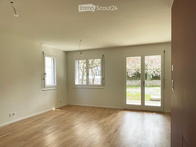 Empty room with wooden flooring, large windows, and sliding glass doors leading to an outdoor area.