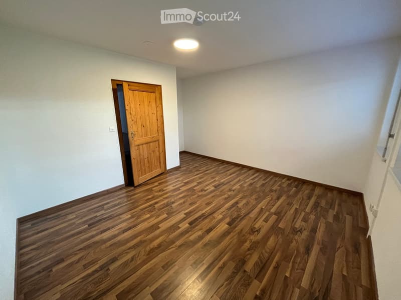 Empty room with wooden flooring, white walls, and a single wooden door leading to another space.