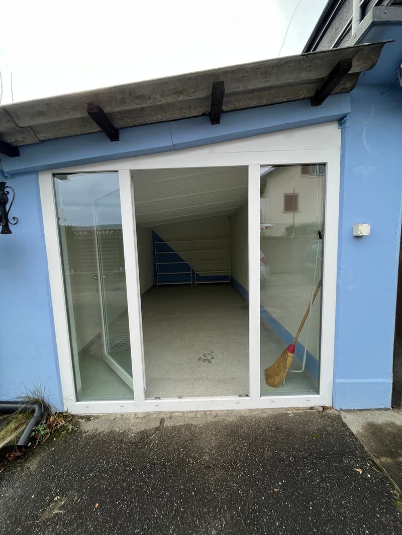 Empty garage with concrete floor, glass doors, and metal shelving units against the back wall.